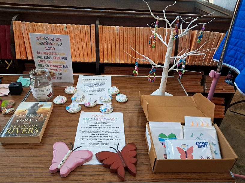 Fundraising display table with orange-spined books, a white decorative bead tree, and a box of greeting cards and butterfly decorations.