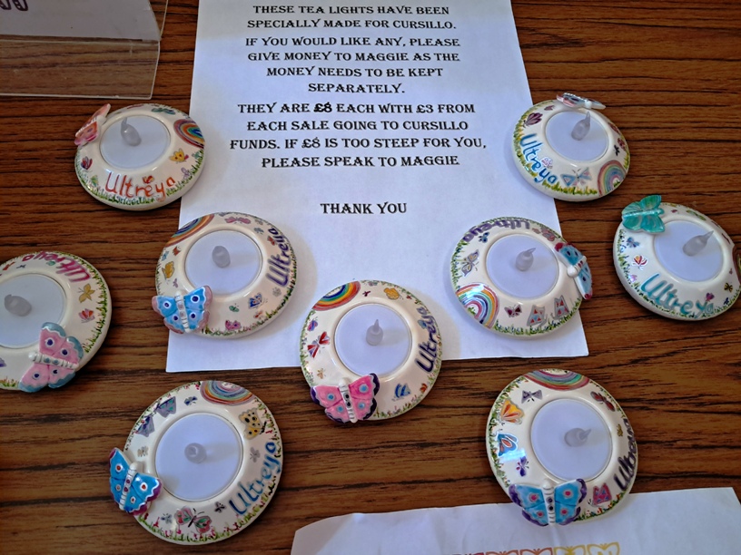Group of ceramic tealight holders with pastel butterfly decorations on a wooden table around a printed notice.