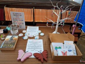 Fundraising display table with orange-spined books, a white decorative bead tree, and a box of greeting cards and butterfly decorations.
